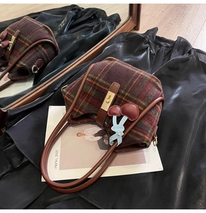 Détail du cabas en laine à carreaux vintage avec lanières en cuir et breloque cerise