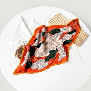 Pleated silk scarf featuring orange floral patterns displayed on a white table set