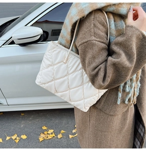 Detail of a creamy white quilted tote bag with diamond stitching shown on a shoulder