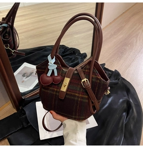 Détail du cabas en tartan avec lanières en cuir, boucles en métal et gri-gri cerise