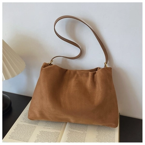 Detail of a brown suede Boston bag with soft pleats on an open magazine