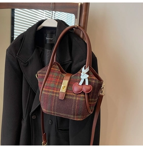 Détail d'un sac cabas rétro en laine quadrillée avec anses en cuir et breloque cerise