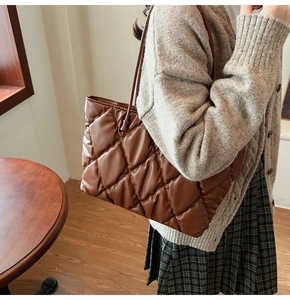 Elegante bolso tote acolchado en cuero marrón llevado por una modelo en interiores