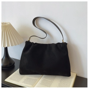 Close-up of black suede Boston bag with soft draped pleats and metal ring details