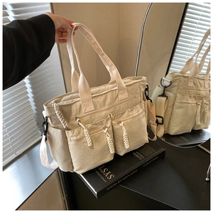 Detailed view of beige multi-pocket tote bag with woven zipper pull and crossbody strap