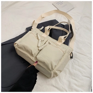 Close-up of cream nylon tote bag featuring multi-pocket design and woven zipper pulls
