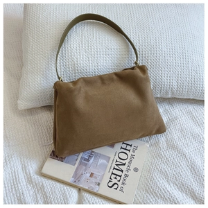 Detail of a brown suede Boston bag with olive green strap on cozy white waffle bedding