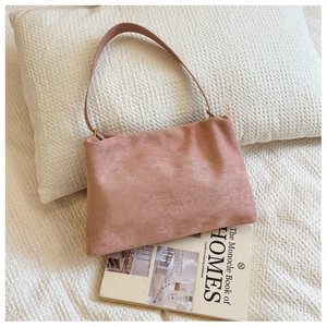 Detail of dusty pink suede Boston bag featuring vintage bronze hardware on a beige texture