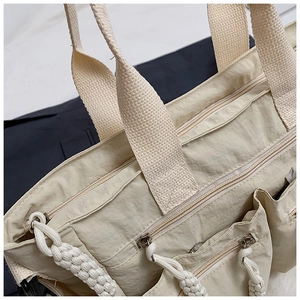 Detail of beige tote bag showing nylon fabric texture and multi-pocket zipper with woven rope