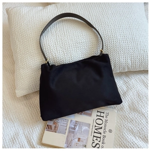 Minimalist black shoulder bag on a white pillow with Monocle book in a lifestyle setting