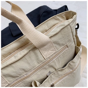 Close-up of beige nylon tote bag showing multiple zipper pockets and reinforced handles