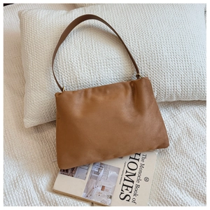 Close-up of brown faux leather Boston bag with vintage gold hardware on white bedding