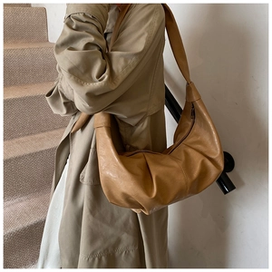 Detail of tan brown pleated leather hobo bag worn with a stylish trench coat