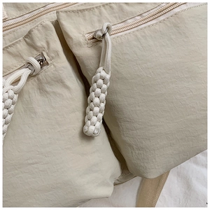 Close-up of beige nylon tote bag featuring multi-pocket design and woven zipper pulls