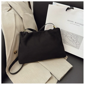 Detail of minimalist black suede Boston bag on beige blazer with golden metal buckles