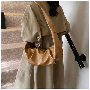 Detailed view of brown leather pleated crescent bag showing texture and drape on model