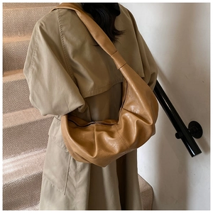 Close-up of a large ginger yellow pleated croissant shoulder bag worn by a model