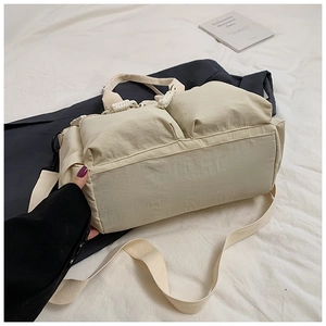 Detail view of beige nylon tote with dual front pockets and thick woven zipper pullers