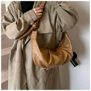 Detail of tan pleated soft leather crescent bag with knot shoulder strap on model