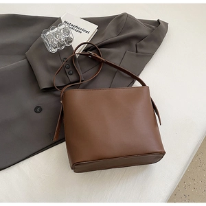 Détail d'un sac seau en similicuir marron posé sur un costume gris au style minimaliste