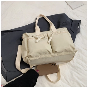Detail of off-white nylon tote bag showing multiple pockets and woven zipper pullers