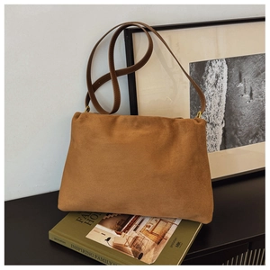 Detail of brown suede Boston bag placed on green books with elegant home decor