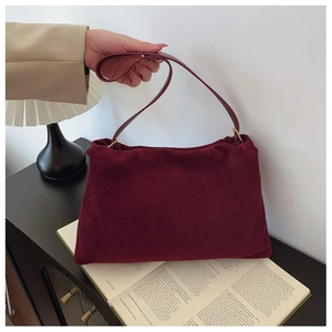 Close-up of burgundy suede Boston bag with golden rings and slim leather handles