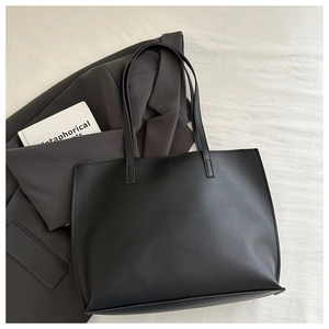 Detail of black tote bag with matte leather texture next to a grey blazer for workwear