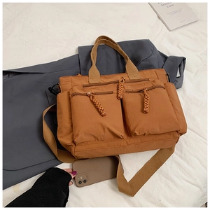 Detail view of brown multi-pocket tote bag with woven zipper pulls and wide strap