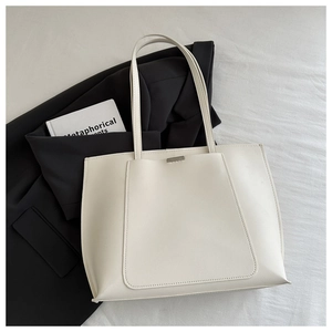 Flat lay of cream faux leather tote bag with silver metal detail on white linen background
