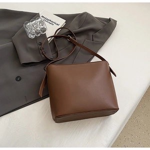 Gros plan détaillé du sac seau en cuir marron sur tissu clair avec des accessoires urbains