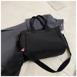 Detail of minimalist black nylon tote showing double handles and adjustable shoulder strap