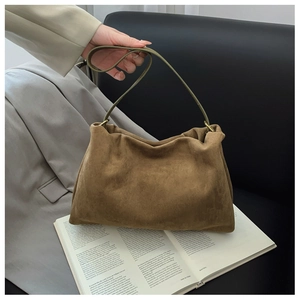 Close-up of a brown suede Boston shoulder bag with green strap on a vintage book