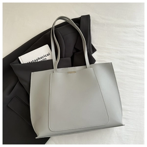 Detail view of large grey tote bag with silver metal bar on a blazer and book background