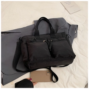 Detailed view of black canvas tote bag featuring double front zipper pockets and straps