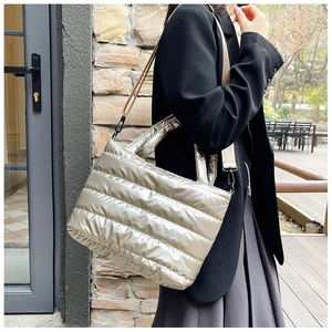 Detail of metallic quilted tote bag worn as a shoulder bag in an urban outdoor setting