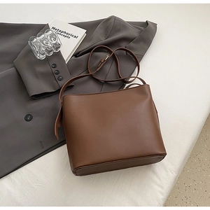 Gros plan d'un sac seau vintage marron foncé porté sur un blazer gris avec accessoires