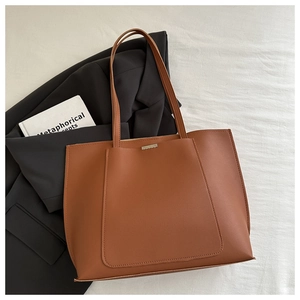 Flat lay of brown leather tote bag with silver metal detail on white fabric background