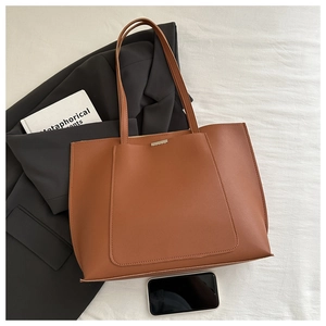 Detail of a brown leather tote bag with front pocket and metal trim on white fabric