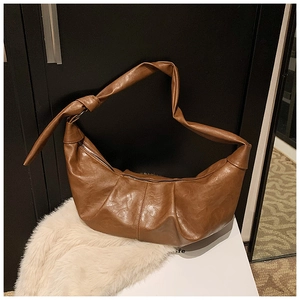 Detailed macro view of the brown crescent bag's textured leather and knotted handle design