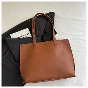 Brown large capacity tote bag displayed on white fabric with a chic black blazer