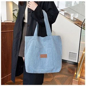 Close-up of light blue textured canvas tote bag with brown leather brand label detail