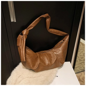 Close-up of caramel brown crescent shoulder bag featuring pleated faux leather and knotted strap