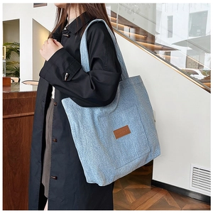 Detail of light blue denim canvas tote bag with a brown leather patch label