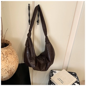 Detail of dark brown pleated hobo bag with knotted wide shoulder strap on a wall hook