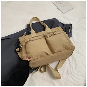 Detail view of khaki nylon tote bag featuring dual front pockets and woven zipper pulls