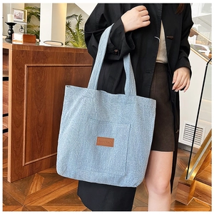 Detail of light blue corduroy tote bag featuring a leather Speed Mail patch and front pocket
