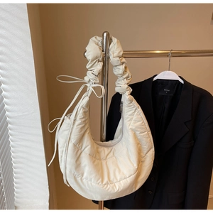 Detail of off-white quilted hobo bag with scrunchie handle and bow detail on a hanger