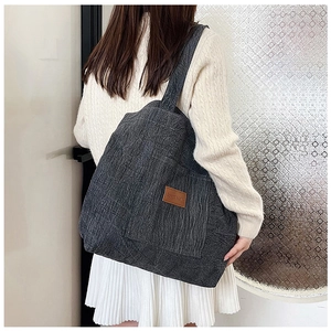 Detail of grey canvas tote bag with brown leather label and wide shoulder strap