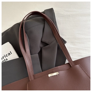 Detail of a brown leather tote bag with a silver metal plate and twin shoulder straps